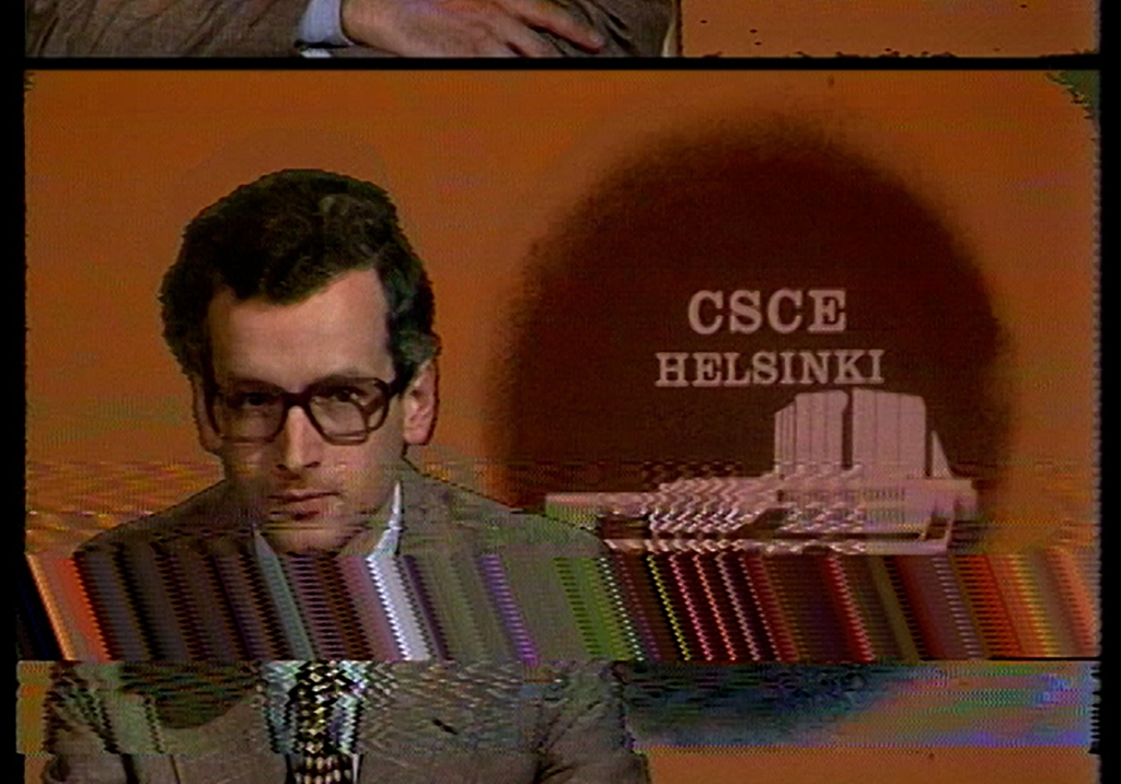 Televisioruudussa uutisten lukija, jonka taustalla teksti "CSCE HELSINKI"