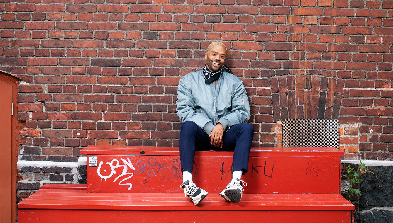 Jani Toivola is laughing and sitting on the red bench in Helsinki. Photo taken by Riitta Supperi.