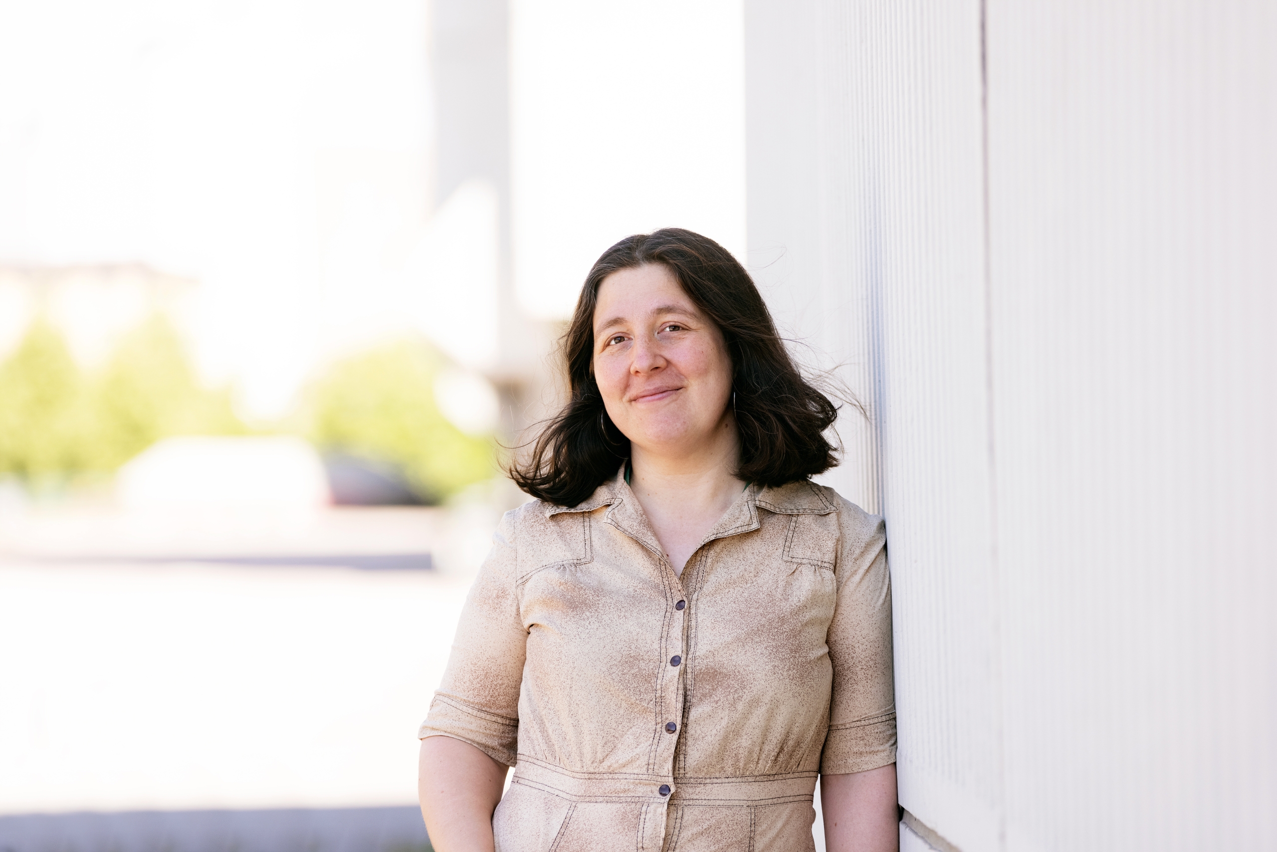 AVEK Award winner 2022 Azar Saiyar leans on a wall outside. She looks directly into the camera and smiles.