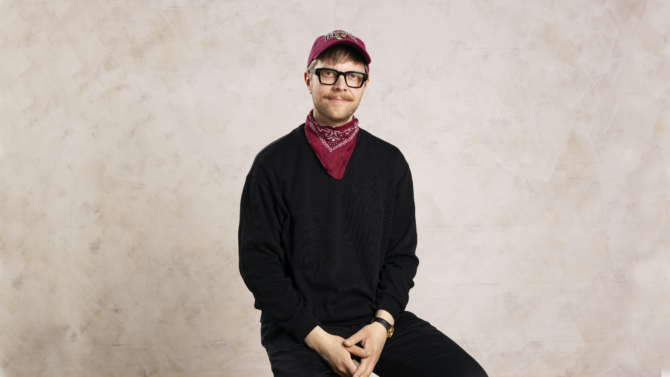 Juho-Pekka Tanskanen istuu, hänellä on kädet sylissään, hän katsoo kameraan. Tausta on vaalea.