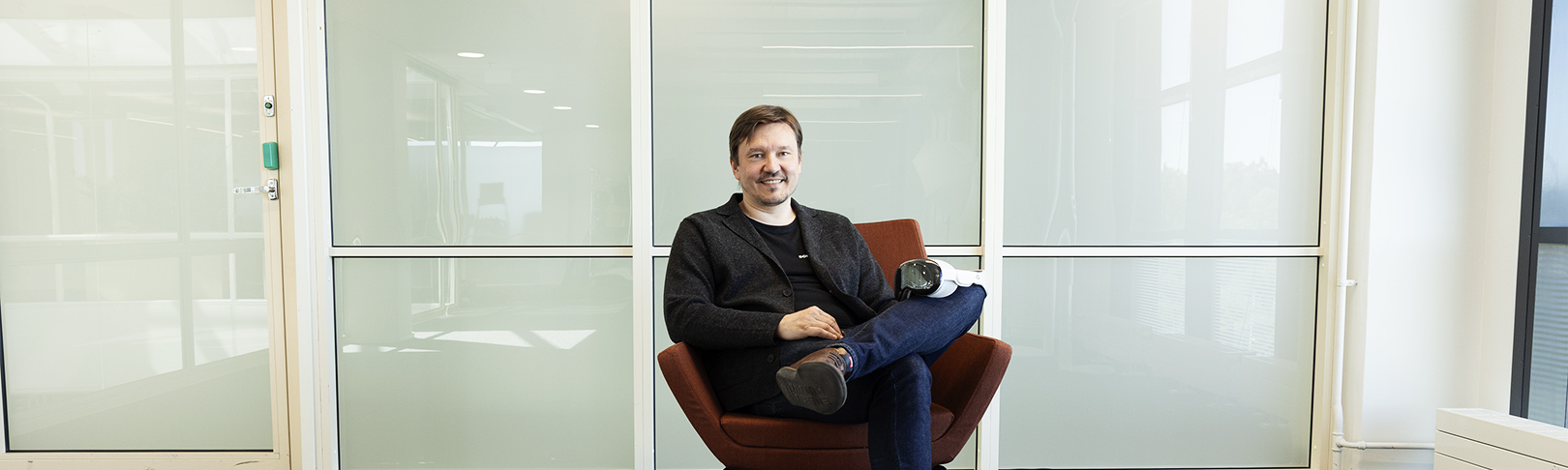 Sami Jahnukainen sitting on a chair. Glass walls in the background.